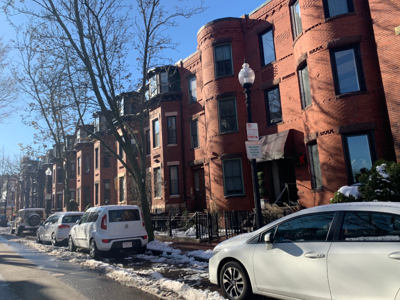 Brownstone homes and parked cars line a city street.